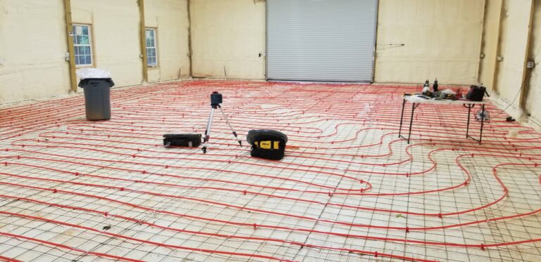 Radiant floor heating system installation with red PEX tubing laid out across concrete foundation before pouring