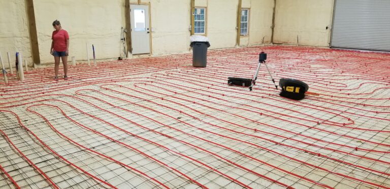 Radiant floor heating system installation with red PEX tubing laid out across concrete foundation before pouring