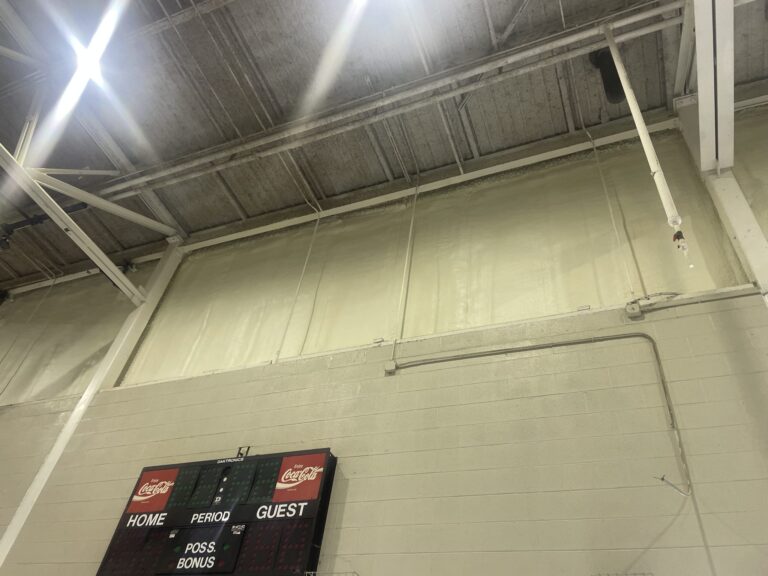 Gymnasium interior wall with spray foam insulation applied above scoreboard for improved energy efficiency